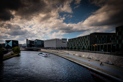 Buildings by river against cloudy sky