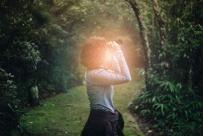 Side view of woman looking through binoculars in forest