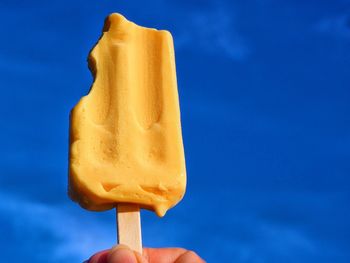 Hand holding ice cream against blue sky