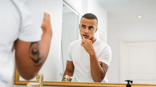 Young man brushing teeth reflecting on mirror in bathroom