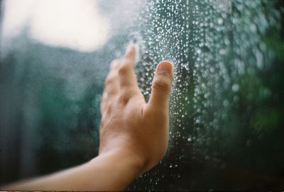 Cropped image of hand touching wet glass window
