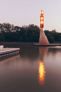 Illuminated lighthouse by lake against sky at night