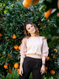 Portrait of young woman standing against tree