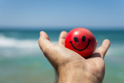 Close-up of hand holding red ball against sea