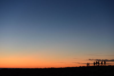 Silhouette people on land against sky during sunset