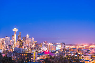 Illuminated buildings in city against blue sky