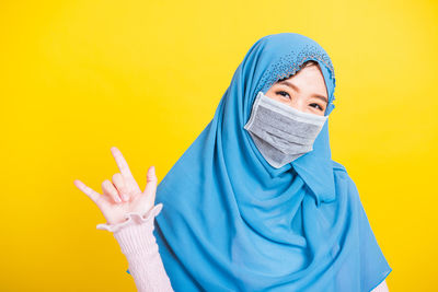 Portrait of young woman wearing mask standing against yellow background