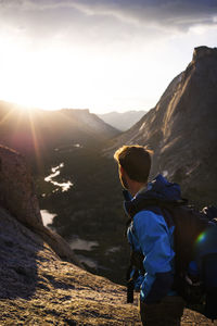 Side view of hiker with backpack standing on mountain against sky