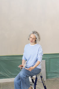 Woman sitting on ladder with tablet pc in front of wall at home