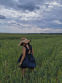 Rear view of woman wearing hat while standing on field against sky