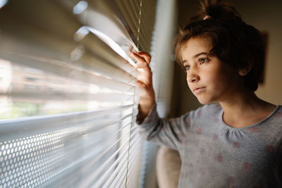 Portrait of girl looking away while standing on window