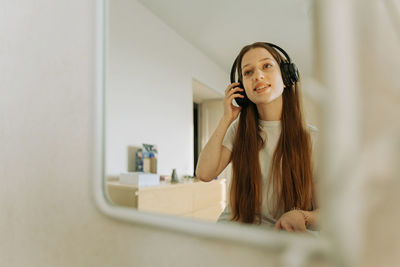 Beautiful teenage girl in headphones singing at the mirror at home