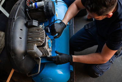 From above of professional mechanic in protective gloves inspecting engine of vehicle while working in repair service workshop