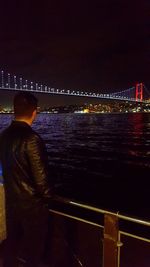 Rear view of man looking at illuminated bridge against sky at night