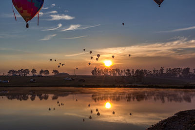 Hot air balloon flying over water against sky during sunset