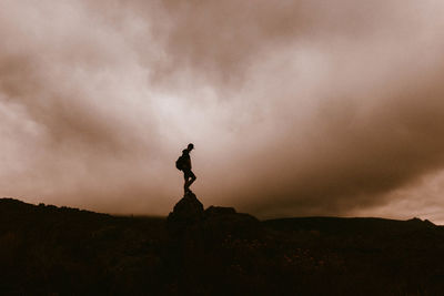 Silhouette man standing on rock against sky