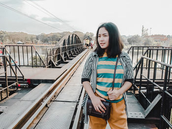 Young woman standing on footbridge against sky