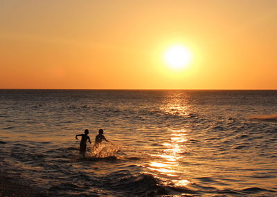 Silhouette people in sea against sky during sunset