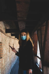 Woman holding mobile phone while standing in corridor