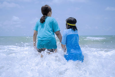 Rear view of friends on sea shore against sky