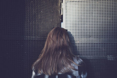 Rear view of woman standing against metal grate