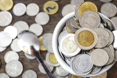 High angle view of coins in bowl by spoon on table