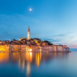 Illuminated buildings by sea against sky at night