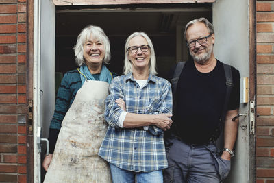 Portrait of smiling senior owners standing at workshop entrance