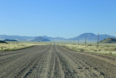 Dirt road amidst field against clear blue sky