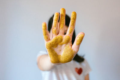 Unrecognizable young girl showing her palm hand covered of golden glitter while doing stop sign