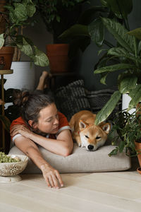Adult woman resting at home with her best furry friend ginger dog in floral nook. biophillia design