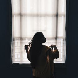 Rear view of woman standing by window at home