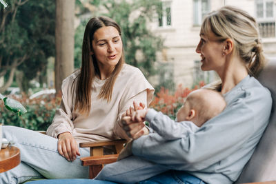 Two women talk about motherhood while nursing a baby while sitting in a cafe.