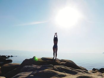 Rear view of seductive woman wearing bikini while posing on rock against sky