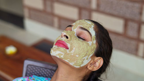 Beautiful young woman using homemade facial mask on face and relaxing at home. multani mitti