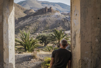 Rear view of adult man standing in doorway of an abandoned building looking at view