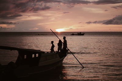 Silhouette people in boat on sea against sky during sunset