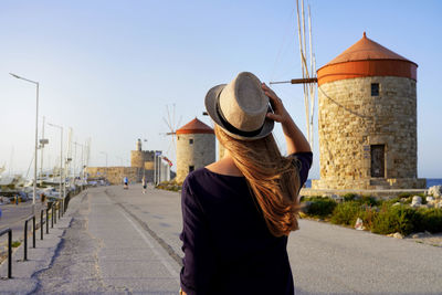 Traveler woman walking along promenade with old windmills of rhodes, europe. sunset.