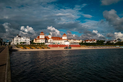 View of buildings by sea against cloudy sky