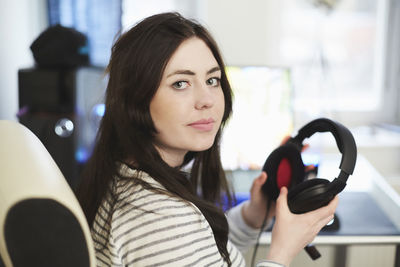 Portrait of young woman holding headphones sitting on chair at home