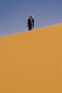 Man on sand dune in desert against clear sky
