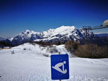 Information sign on snowcapped mountain against blue sky