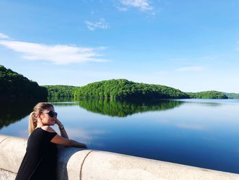 Woman leaning on retaining wall by lake