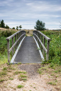 Footbridge amidst trees on field against sky