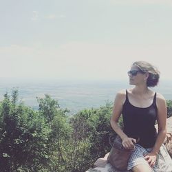 Young woman sitting by sunglasses against sky