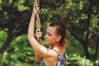 Side view of woman holding rope while standing in forest