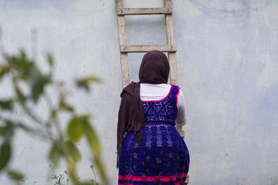 Rear view of teenage girl climbing ladder against wall