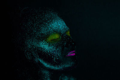 Close-up of woman with glowing face paint against black background