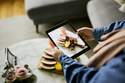 Woman using digital tablet to take photo of food