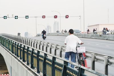 Man with bicycle on bridge against sky